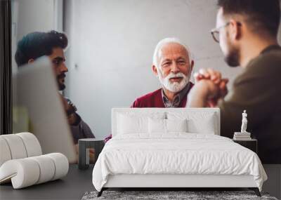 Senior experienced CEO talking to two young employees about business opportunities and company development while sitting in the office. Wall mural