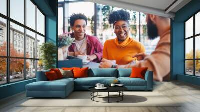 Two guys and a girl sitting in a cafe, talking. The girl is smiling. Wall mural