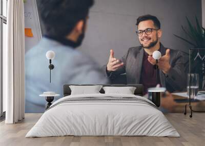 Two young Caucasian entrepreneurs discussing business ideas and strategies while they are sitting in the office. Wall mural