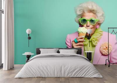 Old senior charming lady in pastel color clothes eat an ice cream on cone. Funny melting scene with food an older aged woman. The background is mint green, copy space. Wall mural