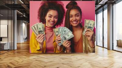 Two joyful women showing off their cash, isolated on a pink background, expressing happiness Wall mural