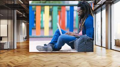 portrait of african man sitting outside with laptop. Wall mural