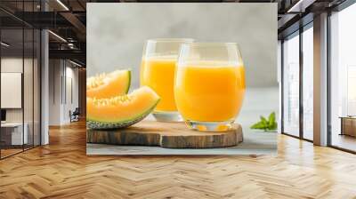 Two glasses of freshly squeezed cantaloupe juice served with cantaloupe slices on a rustic wooden board. Perfect for a healthy and delicious summer drink. Wall mural