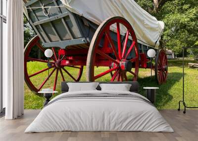 Rear view of a 19th century style horse-drawn carriage or covered wagon set against a green rural nature background. Wall mural