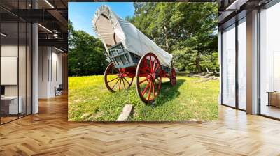 Rear view of a 19th century style horse-drawn carriage or covered wagon set against a green rural nature background. Wall mural