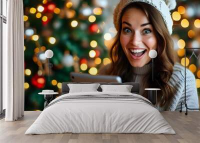 Joyful Caucasian woman thrilled by online gift selection, illuminated by Christmas tree lights, celebrating festive spirit and technology of holiday shopping Wall mural