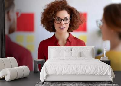 A woman with curly hair and glasses leads a conversation, engaged with two others in a colorful, collaborative environment. Wall mural