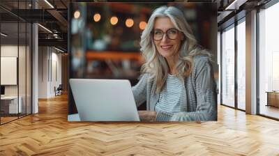 A smiling middle-aged businesswoman sits confidently at the table. The laptop is open in front of you. This is a testament to the power of technology. Bringing people together to achieve shared goals Wall mural