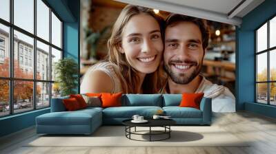 A young woman and her handsome boyfriend smile brightly as they take a selfie at a coffee shop. Their true happiness radiates through the reflection of the joy of their friendship. Wall mural