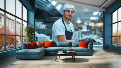 Young man thoroughly cleaning a spotless commercial kitchen with spotless stainless steel counters and shiny appliances under bright lighting. Professional cleaner is scrubbing the surface. Wall mural