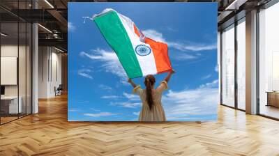 woman standing and holding India flag under blue sky. Wall mural