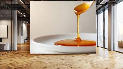 Close-up of honey dripping from a wooden spoon into a white plate, showcasing its rich texture and golden color. Wall mural