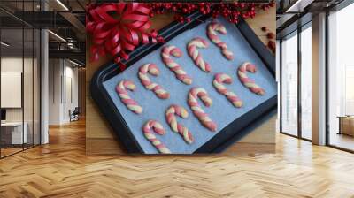 Christmas cookies in shape of a candy cane on a baking tray on a wooden table with festive red decorations Wall mural