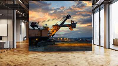 the worker man and yellow excavator loading soil a truck at mine back lit on twilight after sunset Wall mural