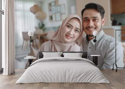 A man and woman are smiling for the camera in a living room. The woman is wearing a hijab and the man is wearing a white shirt Wall mural