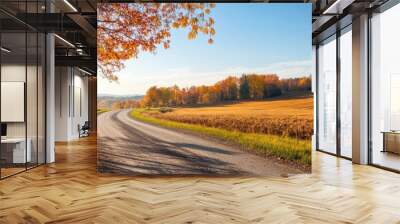 A picturesque autumn landscape featuring a winding road flanked by vibrant trees and golden fields under a clear blue sky. Wall mural