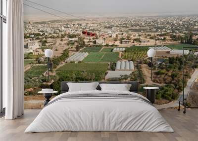 red cable cars going up to the mount of the temptation of jesus in jericho with modern high tech farms in the foreground and the palestinian city in the background Wall mural