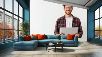 Cheerful young man with eyeglasses holding a laptop standing against a white background, concept of technology and modern freelance work Wall mural