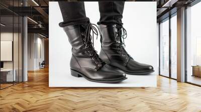 A stylish pair of black lace-up boots worn with black jeans against a plain white background showcasing contemporary fashion Wall mural