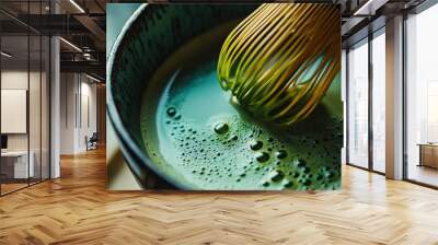 A close-up of a cup of matcha green tea with a bamboo whisk, highlighting the vibrant green color and frothy texture. Wall mural