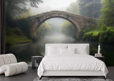 A historic stone bridge arching over a misty river in a peaceful countryside. Wall mural