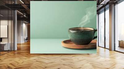 A steaming cup of black coffee on a rustic wood saucer, isolated on a light green background. Wall mural