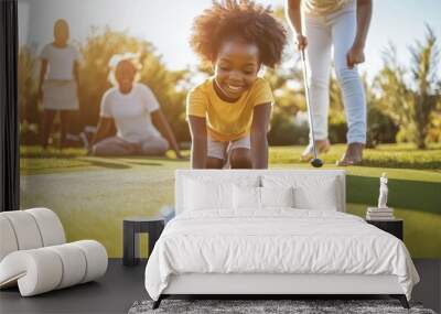 A young girl smiles as she plays on the golf green, practicing her putting with family close by Wall mural