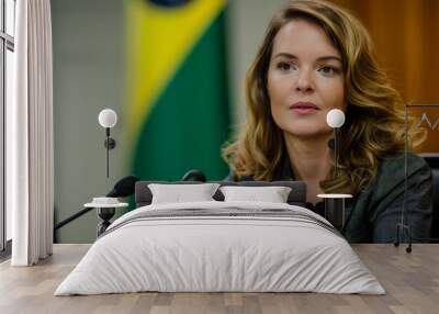 Brazilian woman with light brown hair, speaking to her colleagues during a conference about corporate growth. The background features Brazil's flag on one side Wall mural