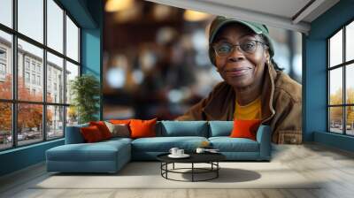 Elderly African woman wearing a green hat and glasses is smiling. Retired black lady is sitting at a table in a restaurant. elderly-african-woman-smiling-restaurant Wall mural