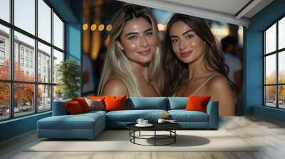 Photograph of two beautiful women friends at an event in Dubai, one blonde with long hair and the other brunette wearing a beige dress, posing for the camera at night time. Wall mural