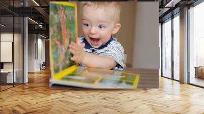 Baby boy turns the page in the book with animal. He is very happy and excited by watching pictures. Child concept. Wall mural