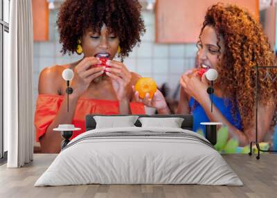 Two black women eating fruits in the kitchen having fun smiling Wall mural