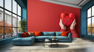 A pair of hands holds a plush heart-shaped gift box against a matching red background, symbolizing love and affection. Wall mural