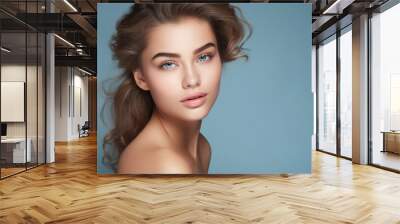 Beautiful young woman with clean perfect skin. Portrait of beauty model with natural nude make up and touching her face. Spa, skincare and wellness. Close up, blue background Wall mural