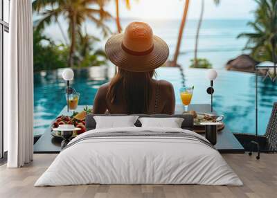 Dinner with sea view in luxury hotel. Woman in straw hat near swimming pool, eating food and enjoy ocean view. Dinner table on tropical vacation. Back view. Concept of travel, holidays, weekend. Wall mural