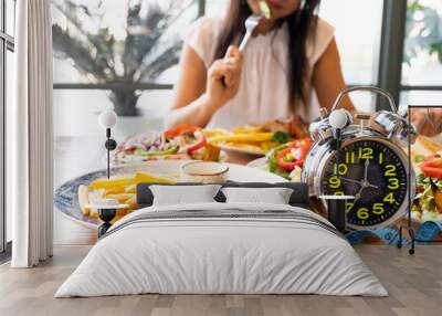 Selective focus of  Alarm clock with woman eating a healthy food as Intermittent fasting, time-restricted eating-Diet breakfast concept Wall mural