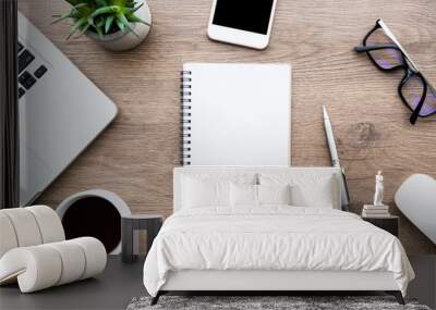 Blank notebook is on top of wood office desk table with lot of things on it. Top view, flat lay. Wall mural