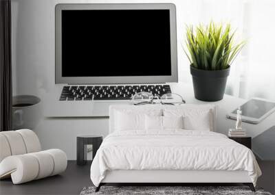 Laptop computer with blank mock up screen is on top of white office desk table with supplies. Wall mural