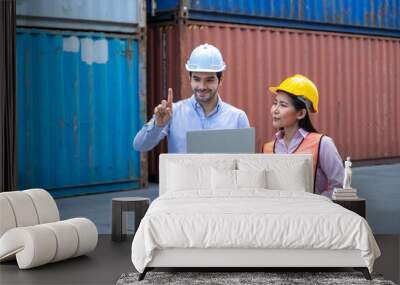 Caucasian shipping officer holding laptop and pointing finger in the air and Asian shipping worker looking at his finger in container shipyard. Wall mural