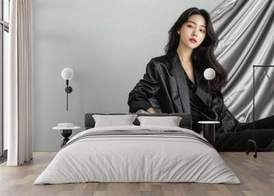 Elegant fashion model with a perfect body wearing a casual black silk jacket and pants sitting gracefully on luxurious silver fabric Wall mural