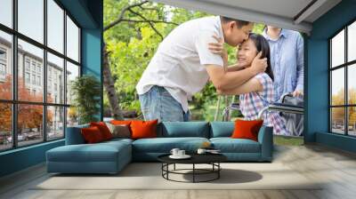 Happy asian family,sick daughter in wheelchair while her father hugging,kiss on the forehead her and mother smiling at park, parent with child girl in summer nature, love family,health care concept Wall mural