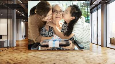 Happy asian mother,daughter meeting old grandparent,giving grandmother a gift,hugging,female elderly hold  present box,woman,child girl visiting senior mother,receiving kisses in cheek from her family Wall mural