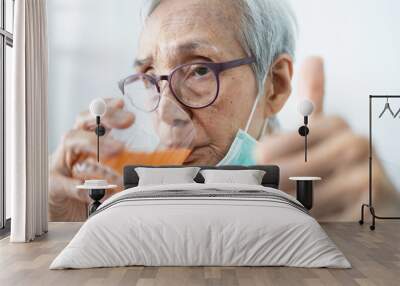 Healthy asian senior woman is drinking a glass of vitamin C or orange juice,elderly people with effervescent vitamin C,strengthening the immunity for cold,flu,fight the Coronavirus,against of Covid-19 Wall mural