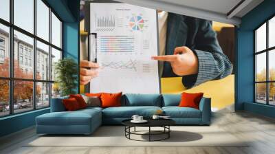 A business professional in a suit presenting a financial summary report with various charts and graphs in an office environment. Wall mural