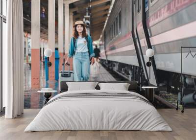 A young woman in casual attire and hat walks with a suitcase on a train station platform, embodying travel and adventure. Wall mural