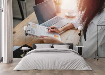 Businesswoman analyzing a marketing report beside her laptop at a wooden desk in a cafe. Wall mural