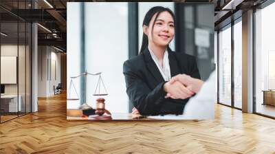 Confident businesswoman in a suit shaking hands with a client, symbolizing successful negotiation or agreement in a professional office environment. Wall mural