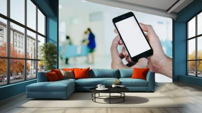 Man hands holding smart phone with blank screen in hospital waiting room, light bokeh background. Wall mural