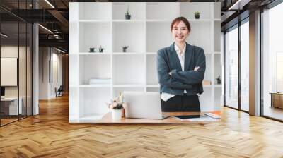 Professional businesswoman standing confidently with arms crossed in a modern office setting, showcasing leadership and success. Wall mural