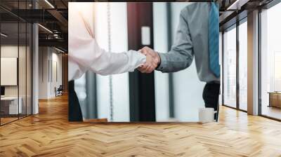 Two business professionals shaking hands in a modern office, symbolizing partnership, agreement, and teamwork. Wall mural